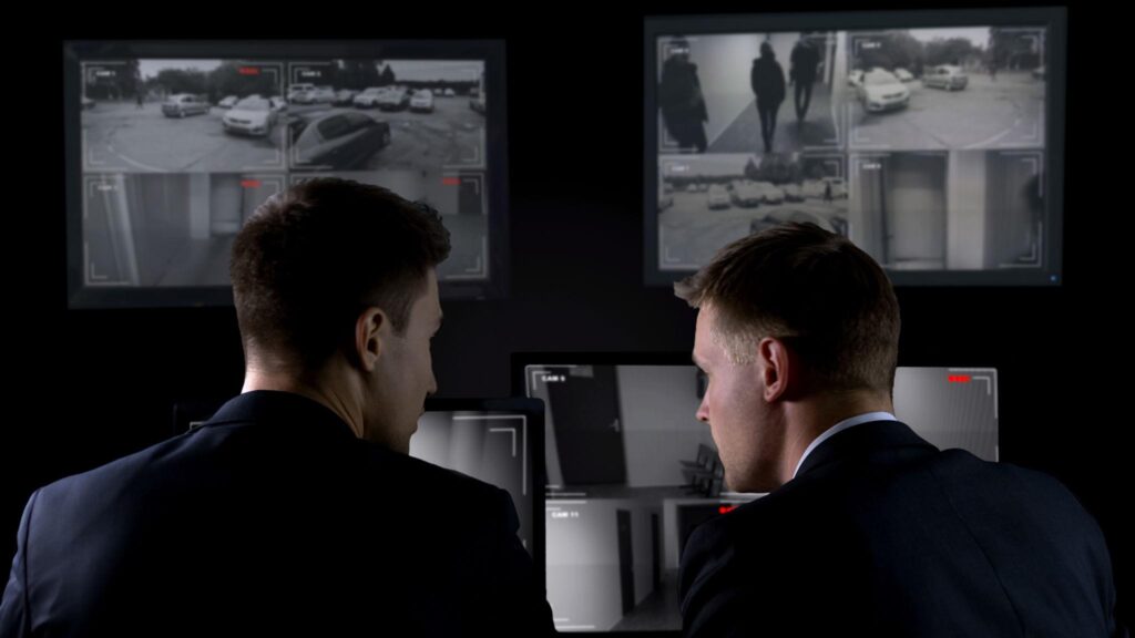 Private investigators observing multiple surveillance monitors during case investigation
